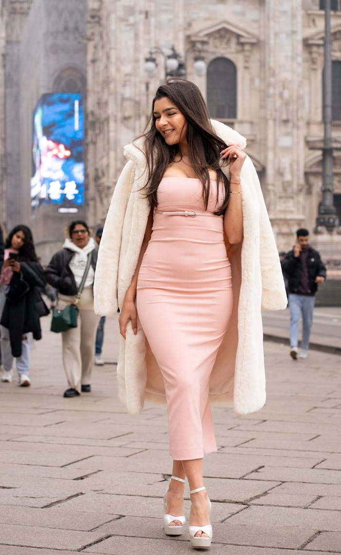 Stylish woman in Milan wearing a chic pink dress and coat, showcasing modern street fashion.