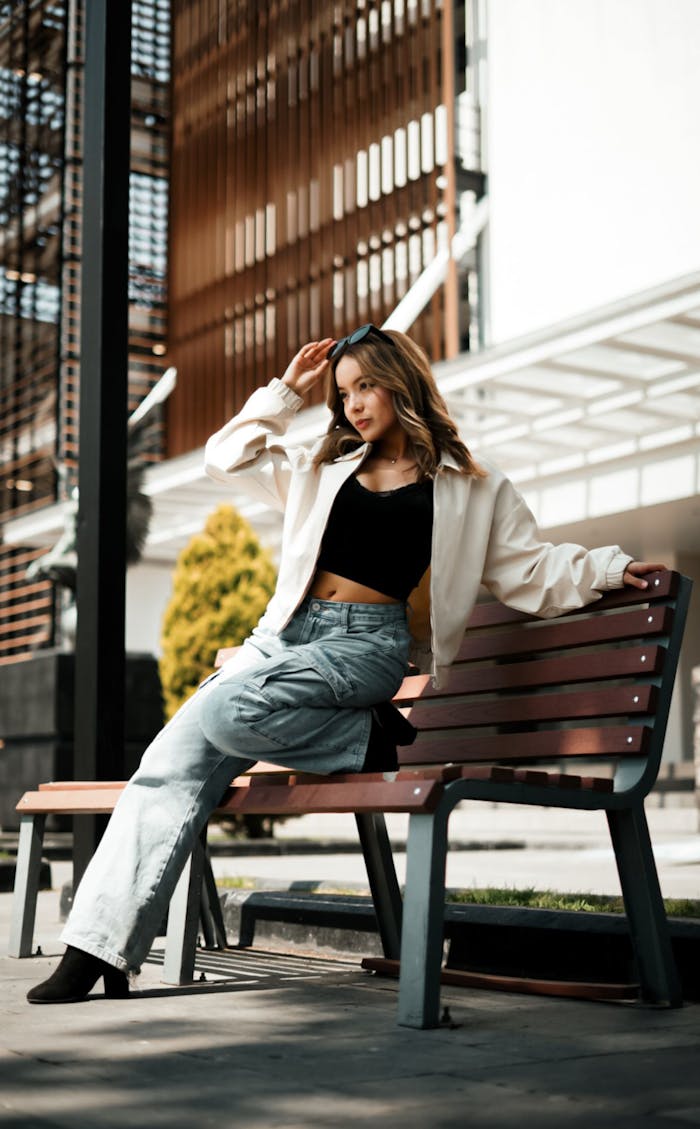 Stylish woman sitting on a bench outdoors in urban setting.